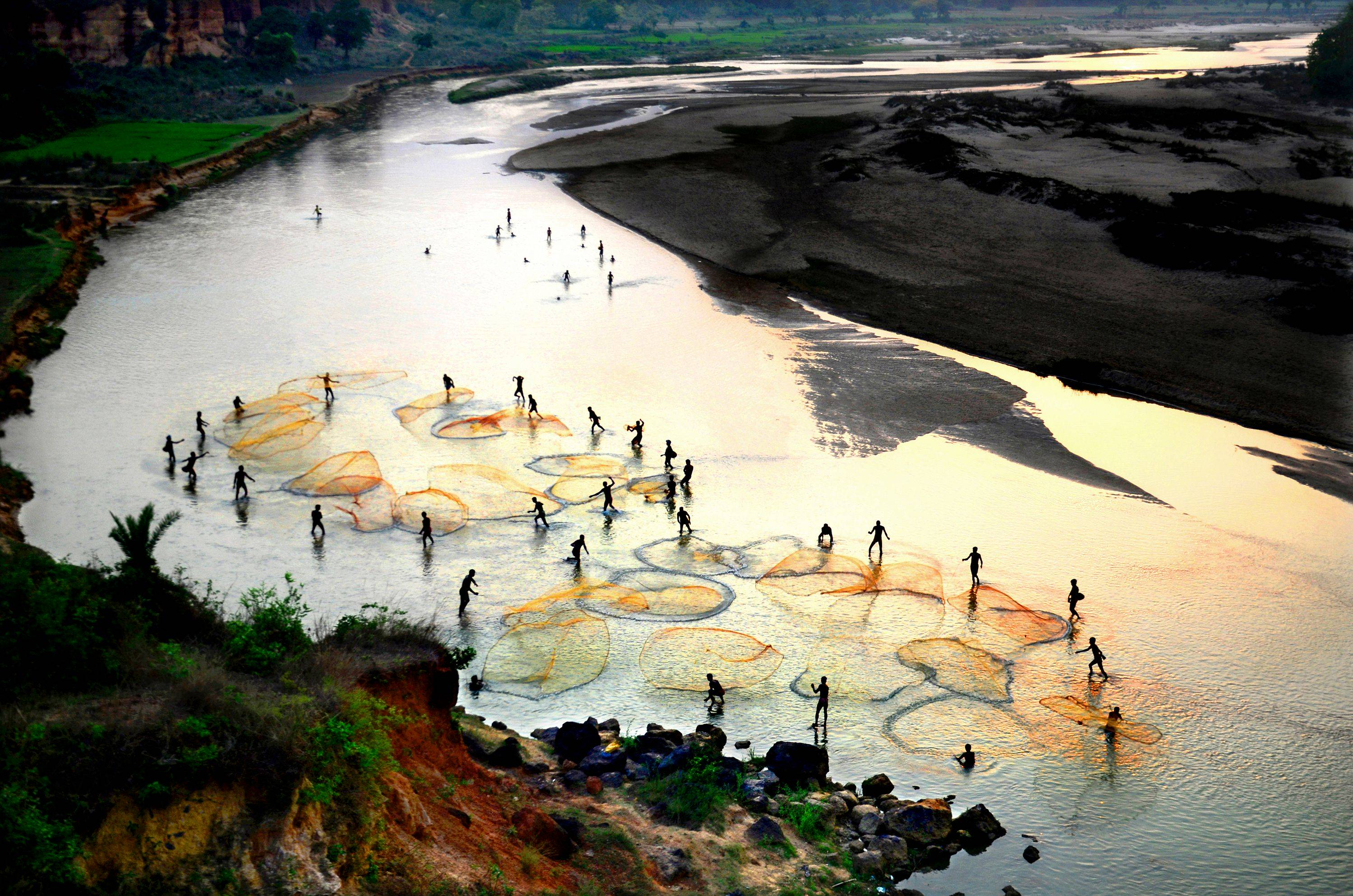 A group of people standing in a river throwing fishing nets.